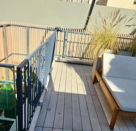 Baranda metálica sobre una terraza con deck de madera y sillón